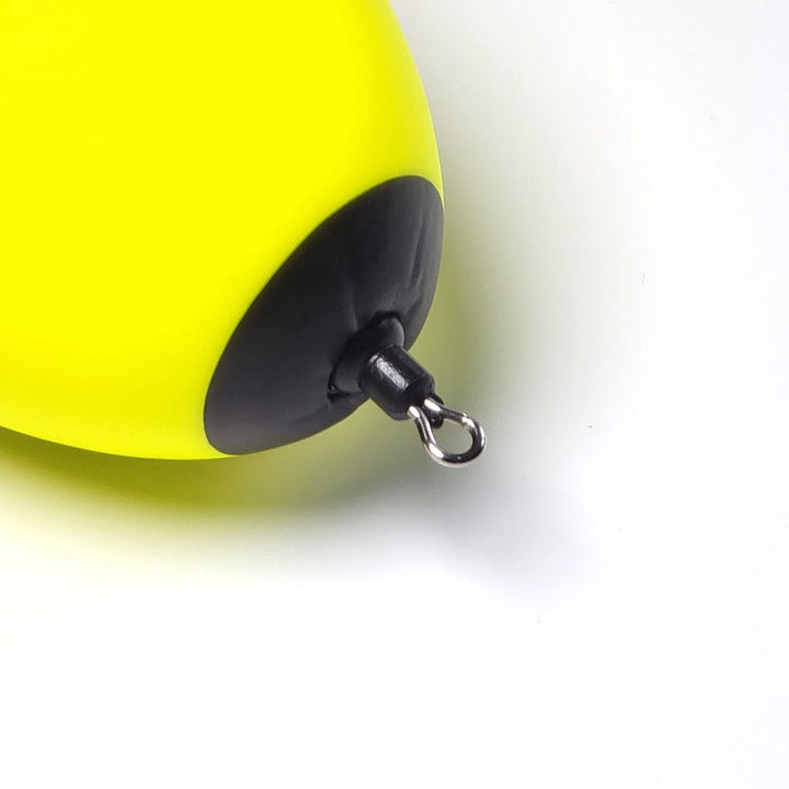 A close-up view of a fishing float. The float is predominantly yellow, with a black bottom section. At the base, there is a small metal loop.